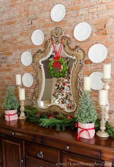 a decorated christmas mantle with candles, plates and a mirror on the wall above it