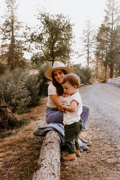 a woman sitting on top of a log holding a small child in her lap and smiling at the camera