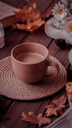 a cup of coffee sitting on top of a wooden table next to leaves and flowers