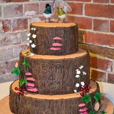 a three tiered cake decorated with mushrooms and flowers on a wooden stand in front of a brick wall