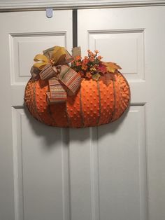 an orange pumpkin decorated with ribbon and bows hangs on the front door's white paneled door