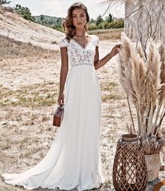 a woman in a white dress standing next to some dried grass and holding a brown purse