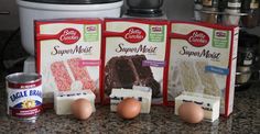 three packages of cake mix sitting on top of a counter next to eggs and other ingredients