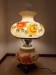 a lamp that is sitting on top of a stand with flowers painted on the lampshade