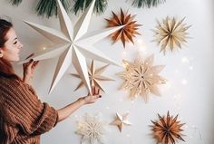 a woman is decorating christmas stars on the wall with gold and white lights,