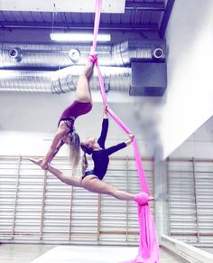 two girls doing aerial acrobatic tricks in an indoor gym with pink ribbons