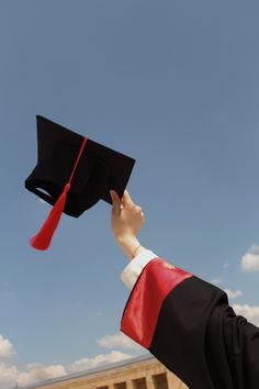 a person in a graduation cap and gown holding up a red tasseled hat