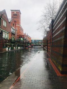 a wet street with brick buildings on both sides and water running down the side walk