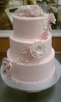 a three tiered wedding cake with pink flowers on the top and white frosting