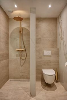 a bathroom with a toilet, shower head and beige tile on the wall next to it