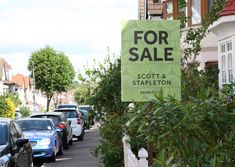 a for sale sign on the side of a street with parked cars in front of it