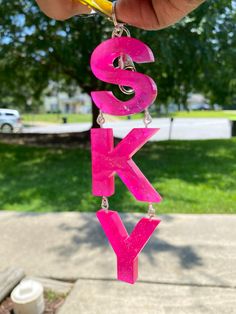 a person holding up a pink letter hanging from a string with the word's k y on it