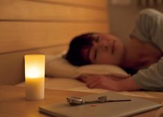 a man laying in bed next to a notebook with a candle on top of it