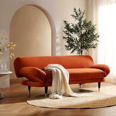 a living room with an orange couch and white rug on the wooden floor next to a potted plant