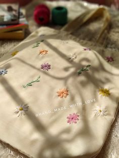 a white bag with flowers on it sitting on top of a bed next to some yarn