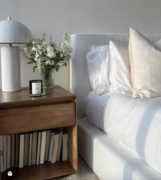 a bed with white sheets and pillows next to a night stand with books on it