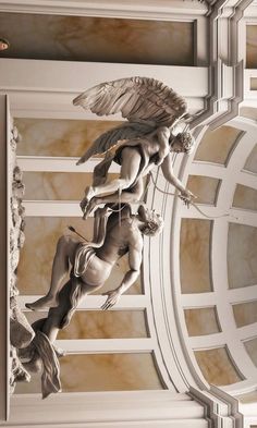 an angel statue hanging from the side of a building's ceiling in front of a clock