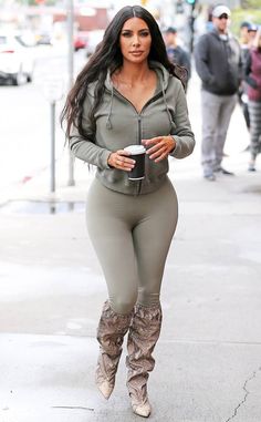 a woman in tight pants and boots is walking down the street with a coffee cup