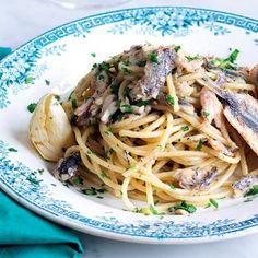 a plate of pasta with fish and parsley on it, next to a glass of wine