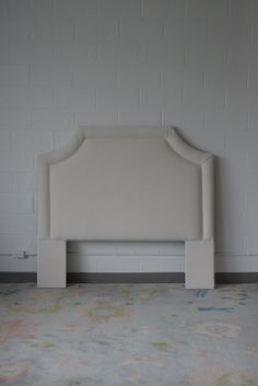 an upholstered headboard against a white brick wall in a room with floral carpet