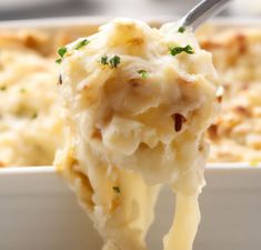 a spoon full of mashed potatoes with parmesan cheese and herbs on top