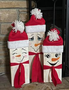 two wooden blocks decorated with snowmen wearing hats and scarfs, standing next to a fireplace