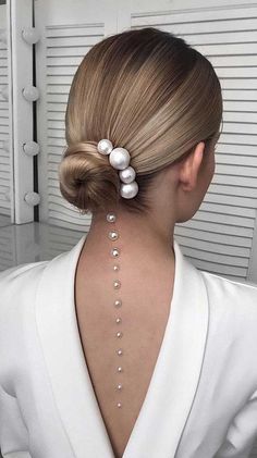 the back of a woman's head with pearls on her neck and behind it is a white jacket