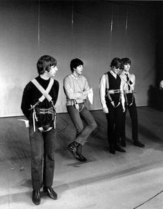 black and white photograph of four young men standing in front of a wall with ropes