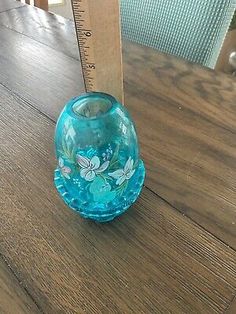 a blue glass vase sitting on top of a wooden table next to a measuring ruler