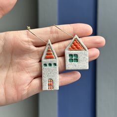 a person is holding two small houses made out of cement blocks and orange tiles on their fingers