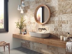 a bathroom with stone walls and a round mirror on the wall, along with a sink