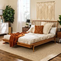 a bed sitting on top of a wooden floor next to a white dresser and potted plant