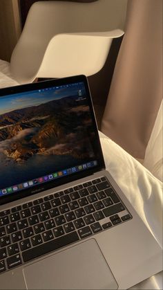 an open laptop computer sitting on top of a white bed next to a chair in a hotel room