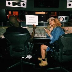 a man and woman sitting in front of a mixing desk holding up a paper sign