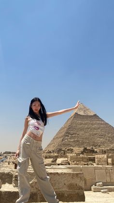 a woman standing in front of the great pyramids with her arms out and one arm outstretched