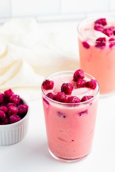 two glasses filled with raspberry smoothie next to another glass full of fruit