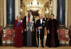 three men and two women in formal dress standing next to each other near a chandelier