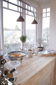 a kitchen counter with plates and bowls on it next to two large windows that look out onto the outdoors