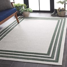 a rug with green and white stripes on the floor in front of a chair, potted plant and window