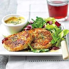 two crab cakes on a plate with salad and dipping sauce