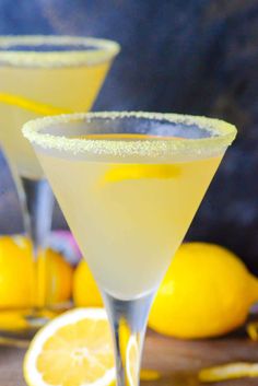 two glasses filled with lemonade sitting on top of a wooden table next to sliced lemons