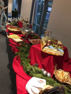 a buffet line with various foods on red table cloths and silverware in front of large windows