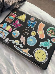 an open laptop computer sitting on top of a white bed covered in sticker sheets