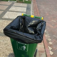 a green trash can sitting on the side of a road next to a brick sidewalk