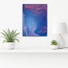 an abstract painting in blue and purple on a white shelf next to two potted plants