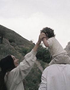 a woman holding the hand of a child on top of her head while walking up a hill