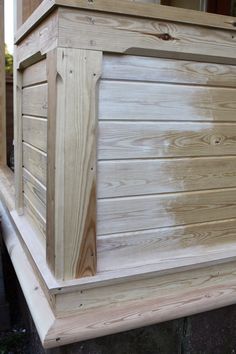 a wooden box sitting on top of a porch next to a building with siding being applied