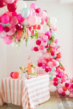 a table topped with balloons and cake next to a tall tree filled with pink, white and red balloons