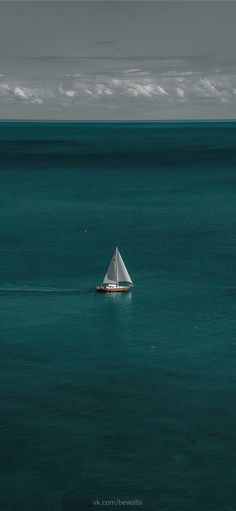 a lone sailboat in the middle of an ocean with dark blue water and white clouds