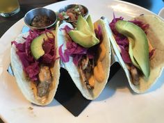 three tacos on a plate with salsa, avocado and other condiments